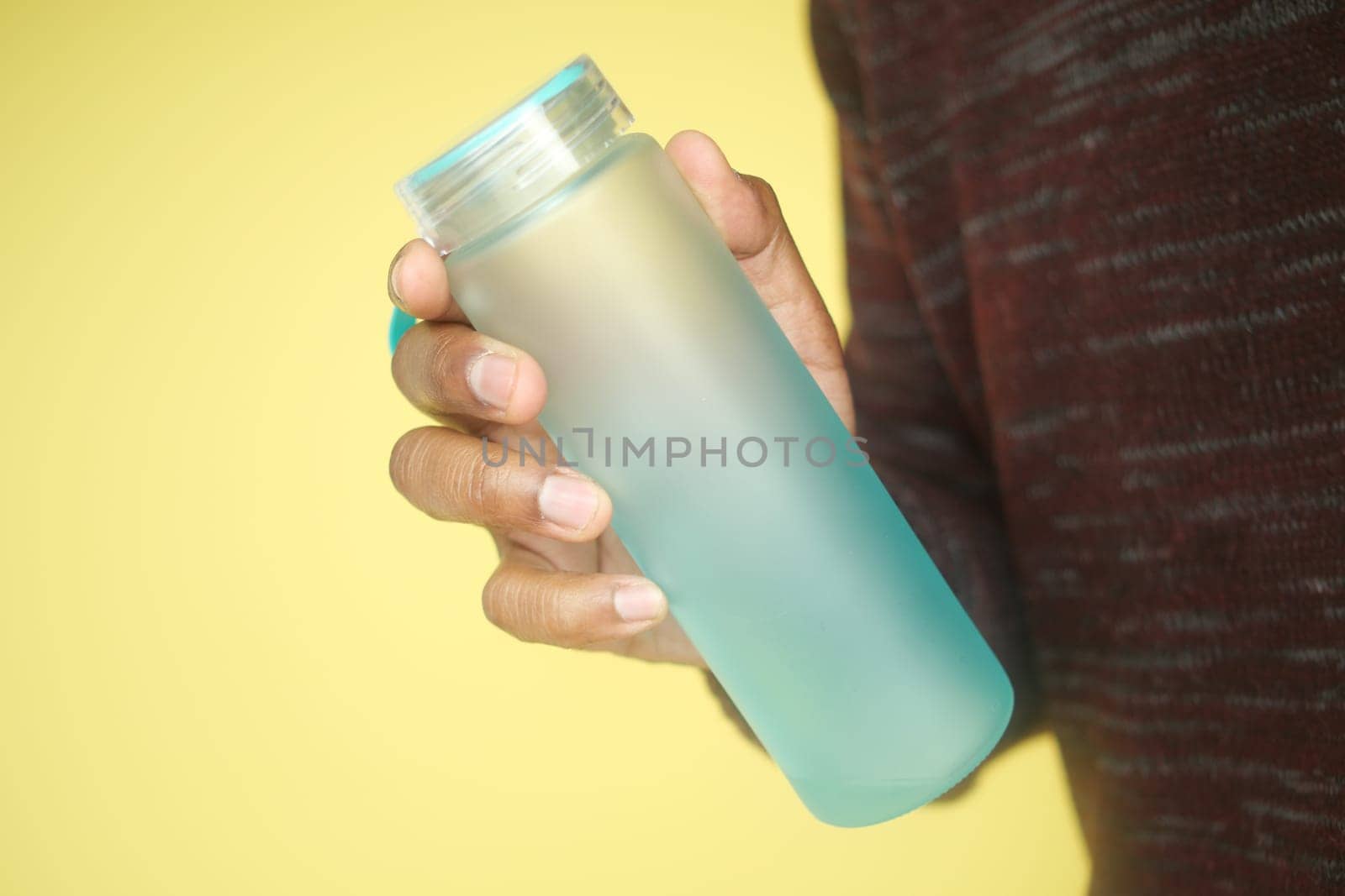 A person holds a frosted water bottle in front of a vivid background.