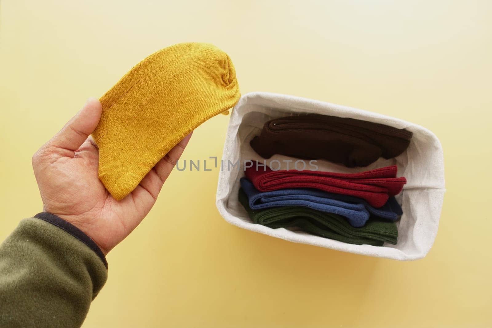 A hand holds a yellow sock while sorting through a basket of colorful socks.