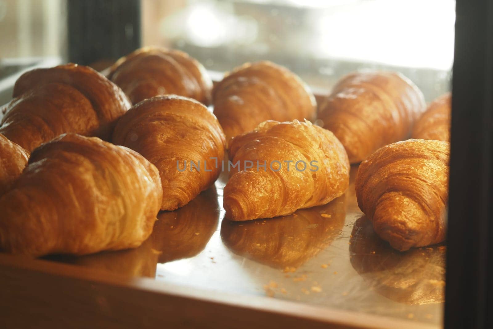 Warm, golden croissants are neatly arranged in a bakery display case.