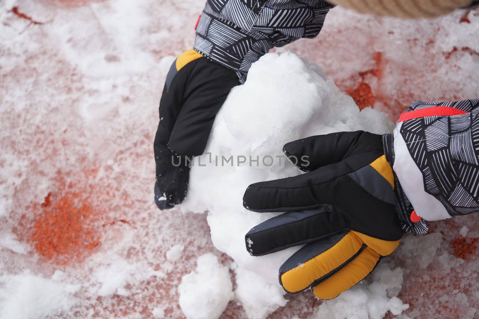 A child is forming a snowball with gloved hands in winter.