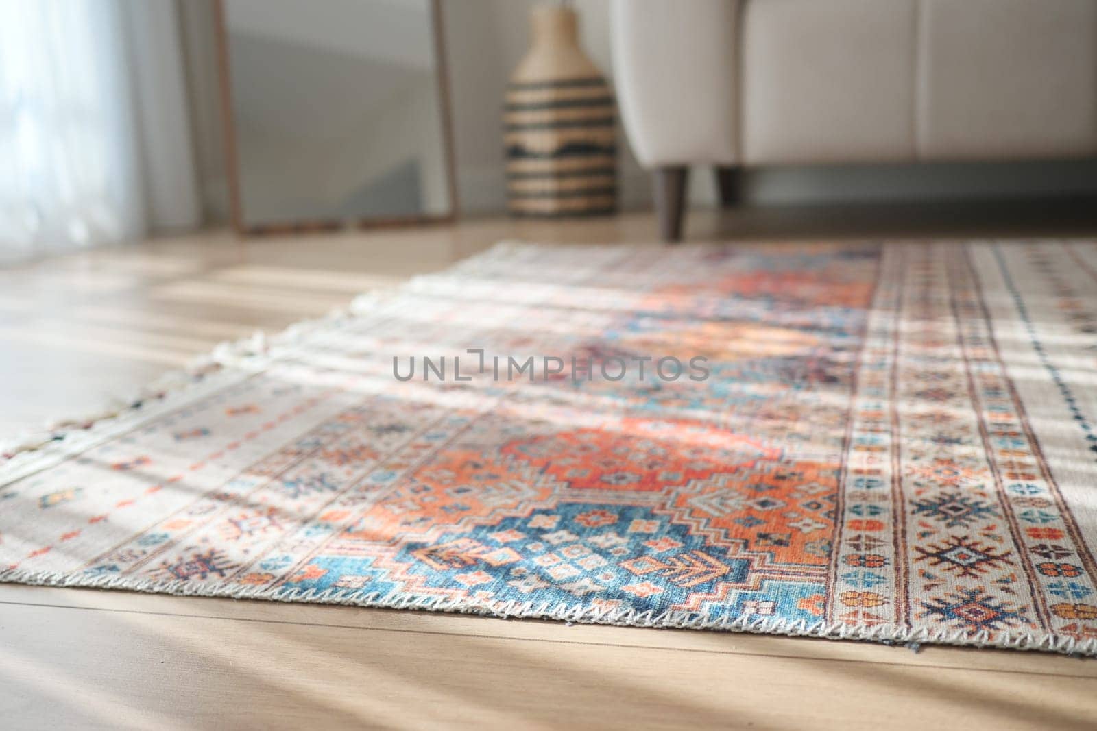 Brightly designed rug lies on a wooden floor beside a couch.