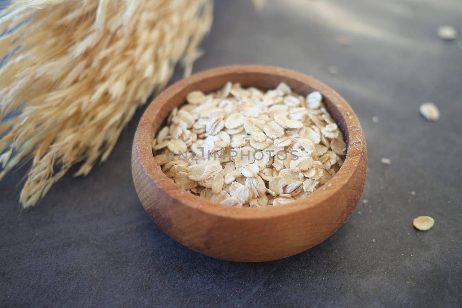 Rolled oats are displayed in a small wooden bowl beside dried grass.