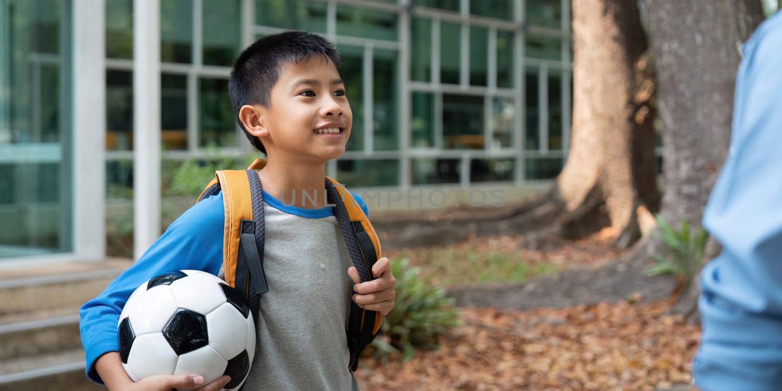 A cheerful young boy with a backpack and soccer ball smiles at a nearby adult, excited for his school day ahead. The setting is bright and welcoming, reflecting the joy of new beginnings.