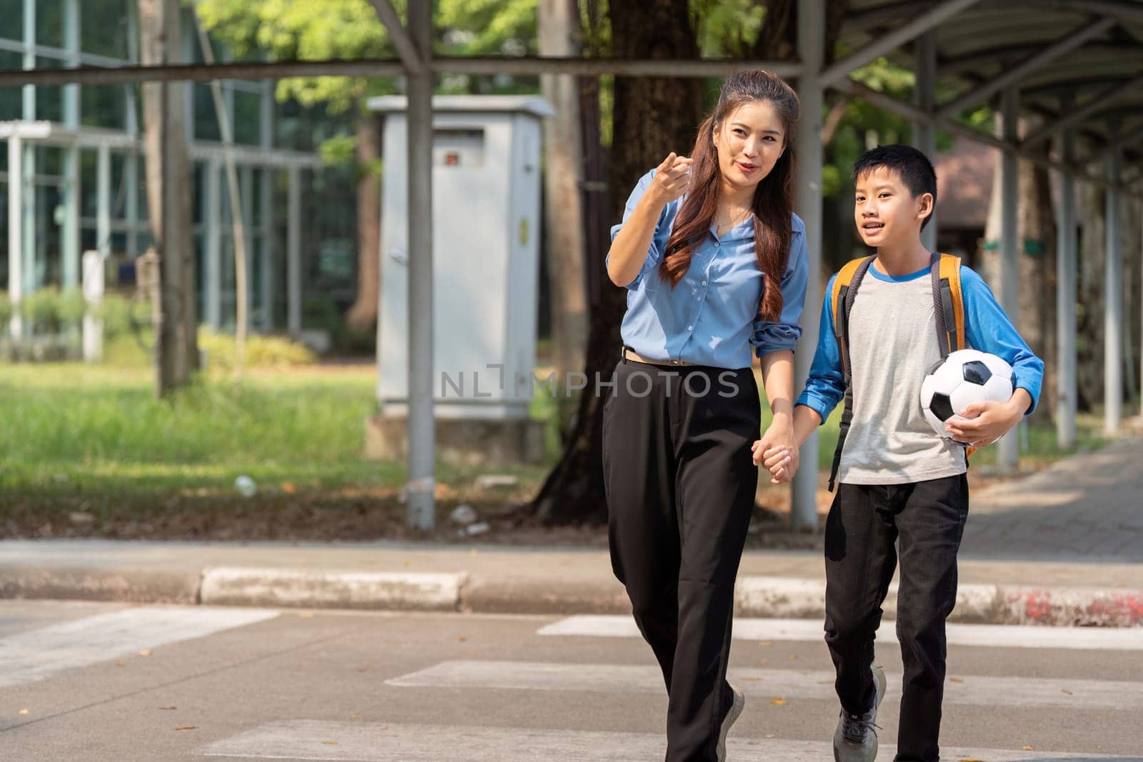 A happy moment as a mother holds her son hand, both excited for the school day ahead, with a soccer ball by their side.