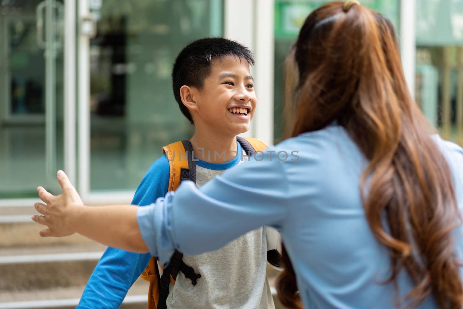 After a long day of school, a young boy with a backpack joyfully approaches his mother, radiating excitement about returning home together.