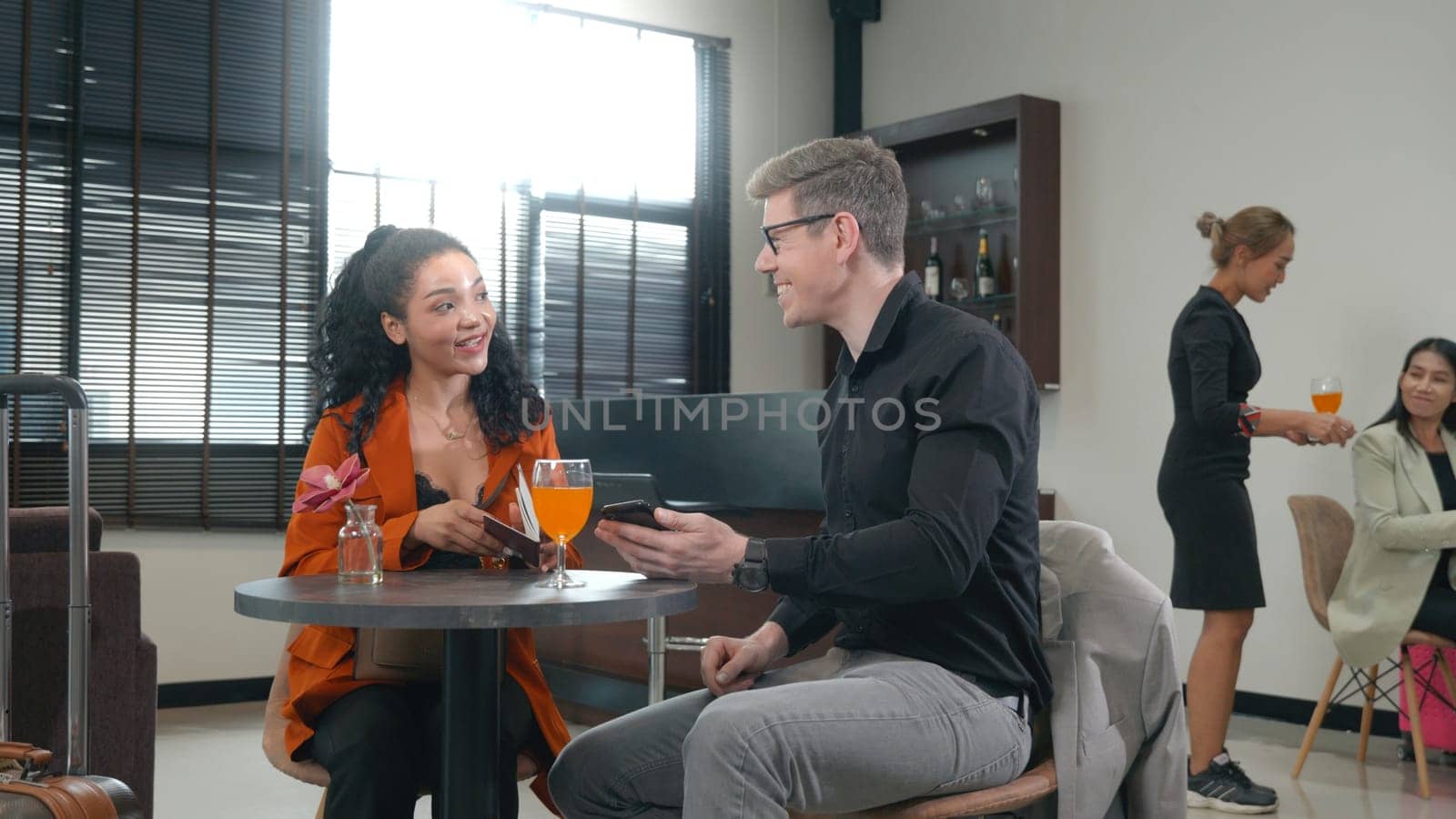 Two elegant partners sitting in airport lounge or waiting room, businessman and woman with suitcase come to meeting and talking together on business travelers waiting their flight at airport terminal