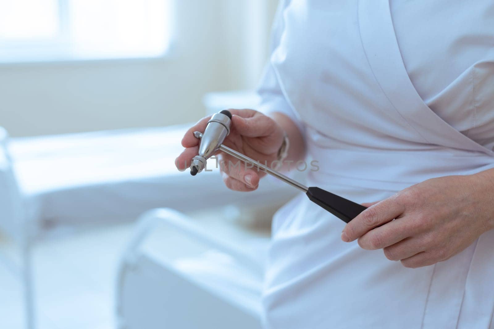 Doctor holding a reflex hammer in a medical room, preparing for neurological examination of a patient.