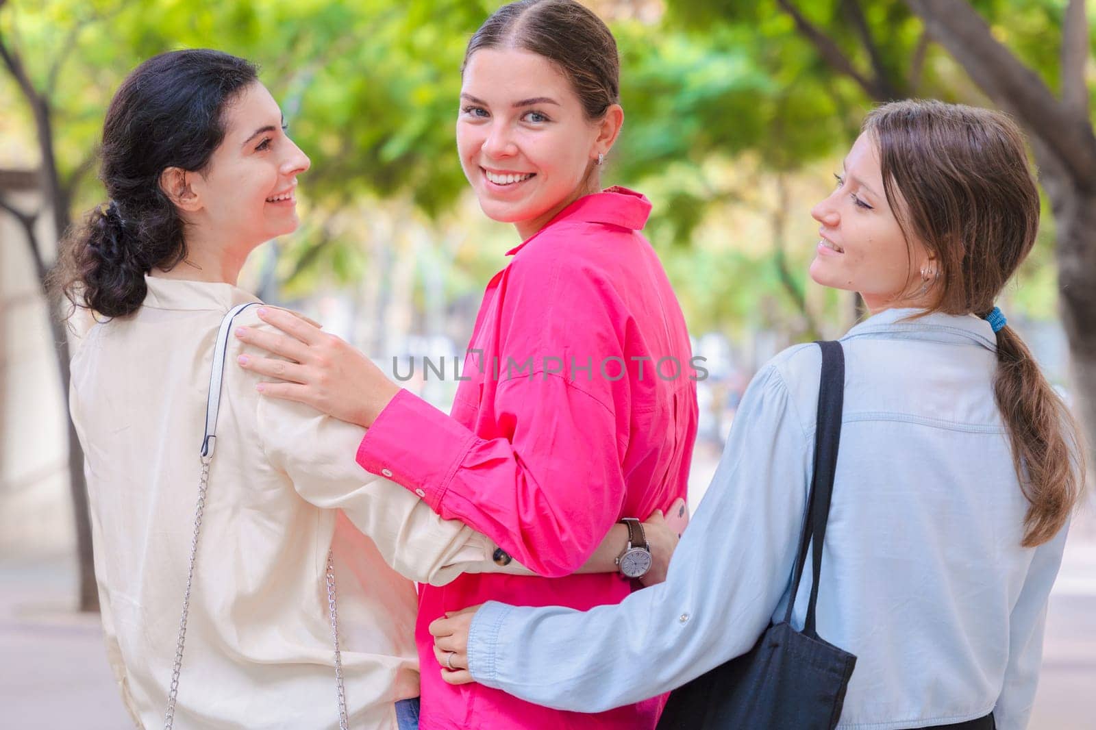 Three Caucasian women walk outdoors, smiling and enjoying a casual moment together. Their relaxed vibe, friendship, and cheerful energy are captured in a bright, tree-lined environment.