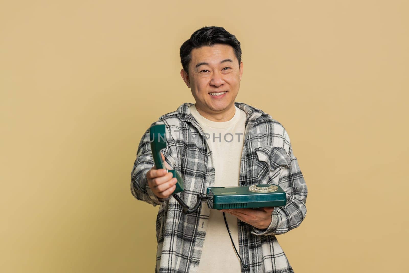 Hey you, call me back. Asian middle-aged man talking on wired landline vintage telephone of 80s advertising proposition of conversation, online shopping. Mature Chinese guy on beige background indoors
