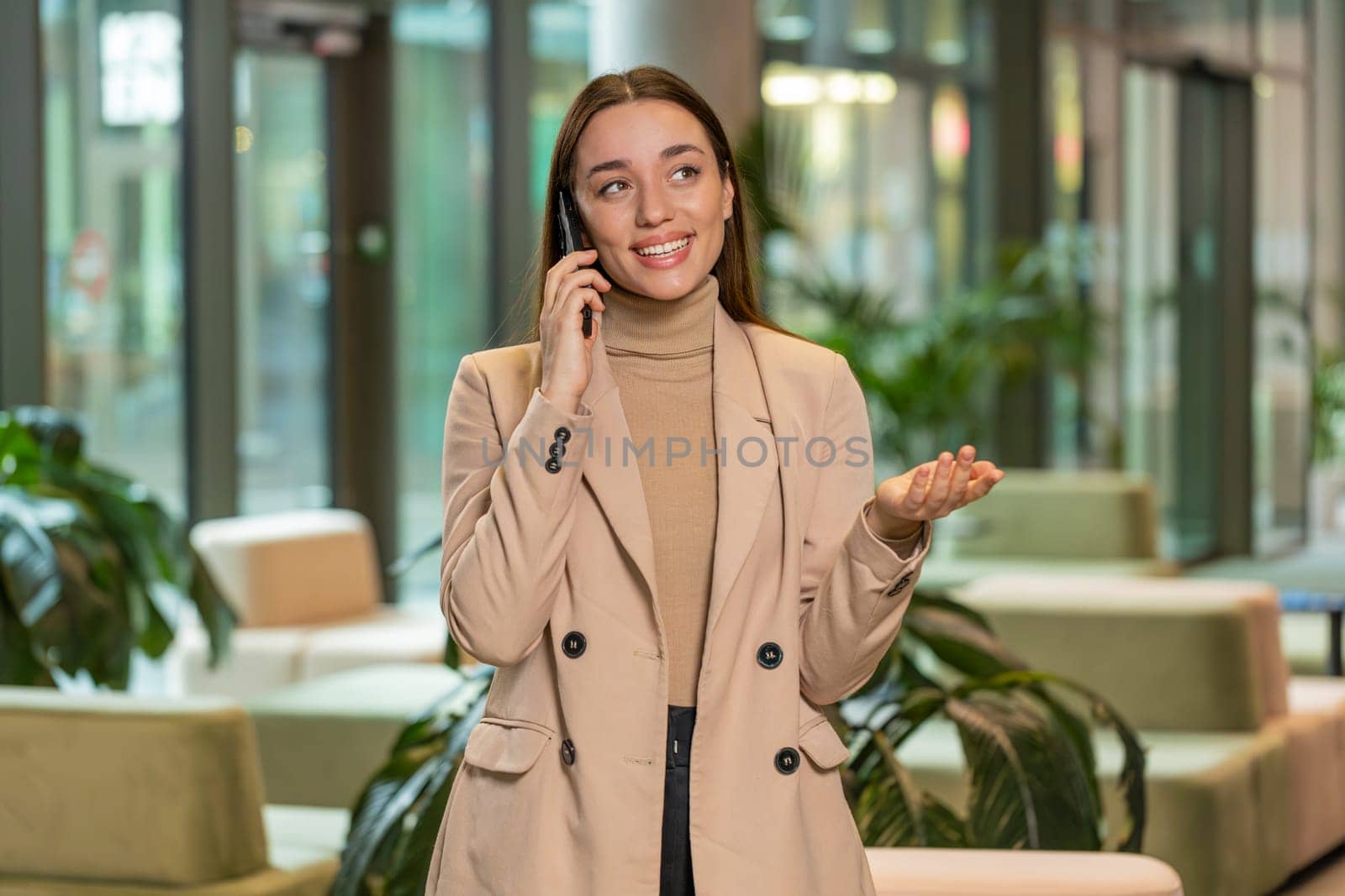 Smiling young businesswoman in formal working, having mobile phone talk in modern office lobby. Professional manager woman girl holding smartphone using messenger chat apps. Employment, occupation.