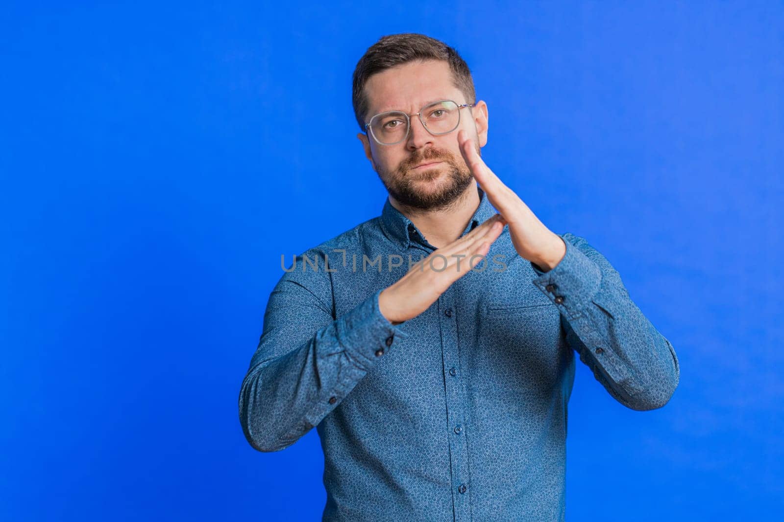 Tired serious upset Caucasian middle-aged man showing time out gesture, limit or stop sign, no pressure, I need more time, take a break, relax, rest, help. Young adult guy isolated on blue background