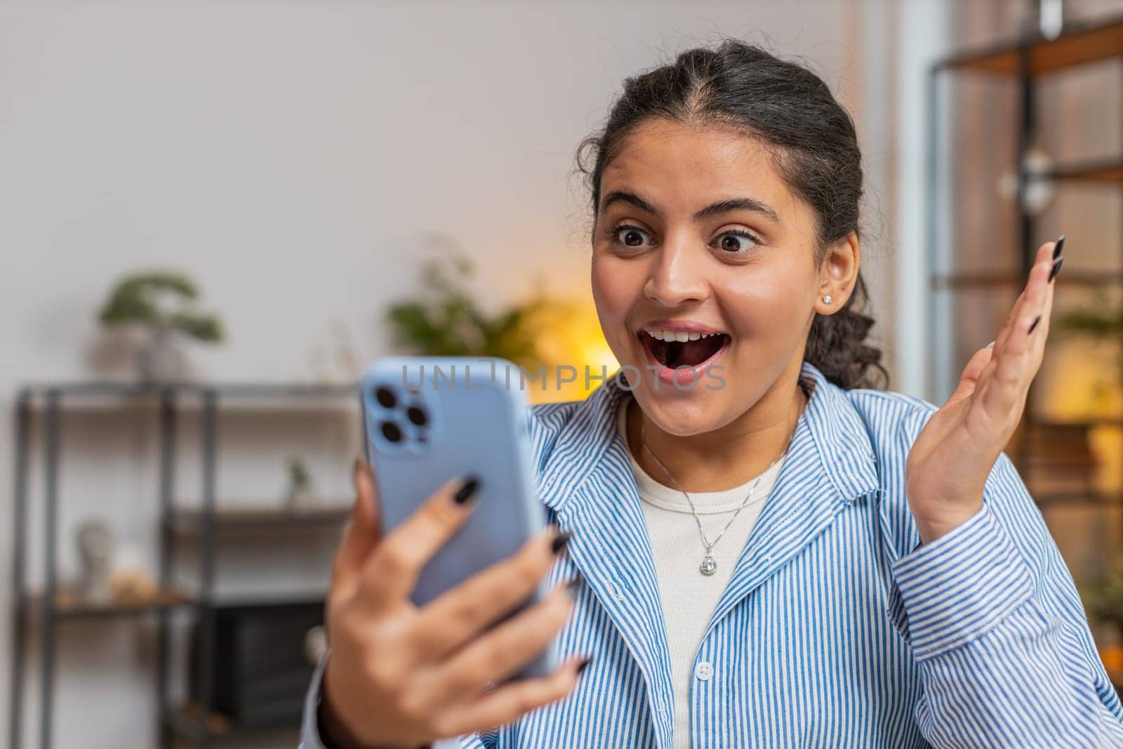 Oh my God Wow. Excited happy joyful winner Caucasian woman use smartphone typing browsing found great win good news celebrate victory. Girl with mobile phone at home office table workplace. Lifestyle.