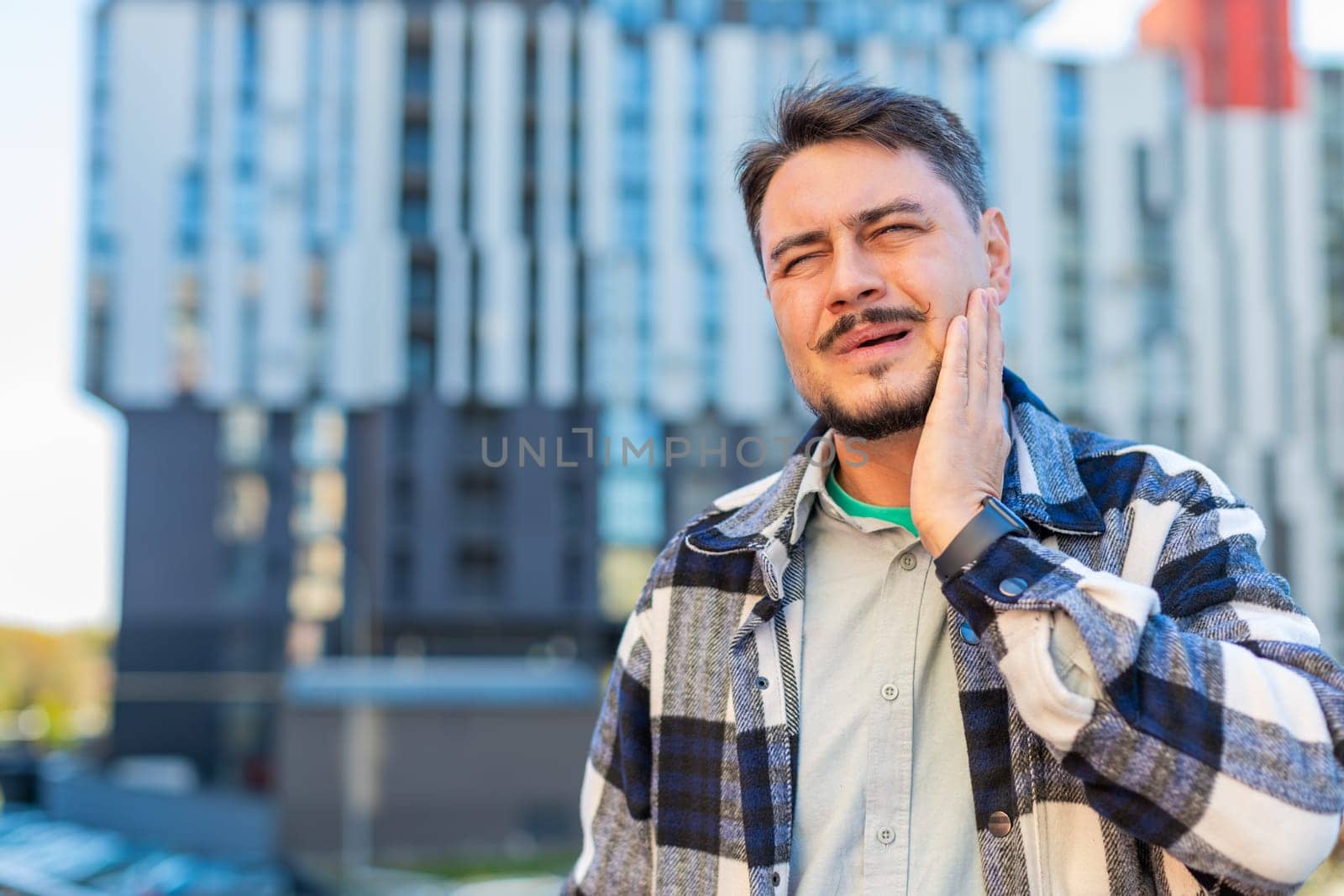 Mature Caucasian man tourist standing on downtown city street feeling toothache bad unpleasant symptoms, guy suffering from pain holding hand on cheek jaw damaged dental nerve needs medical help.