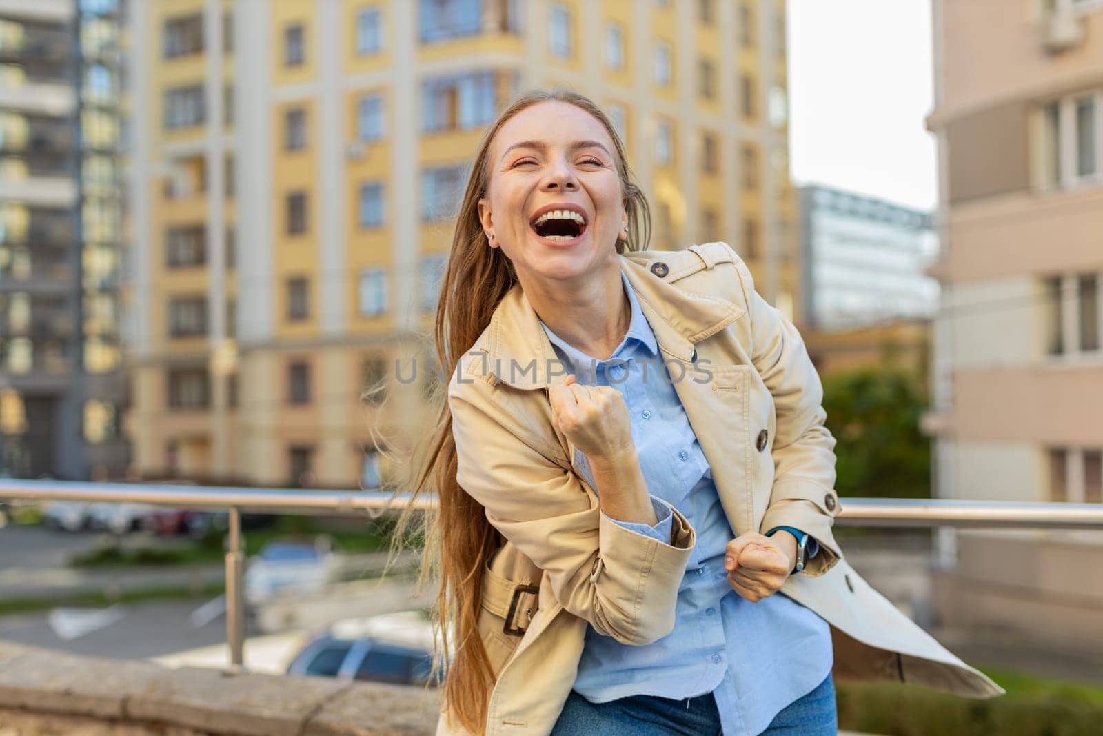 Oh my God, wow. Caucasian mature woman looking surprised, shocked by sudden victory, game winning, lottery goal achievement, good news outdoors. Excited girl clenching fists on downtown city street.