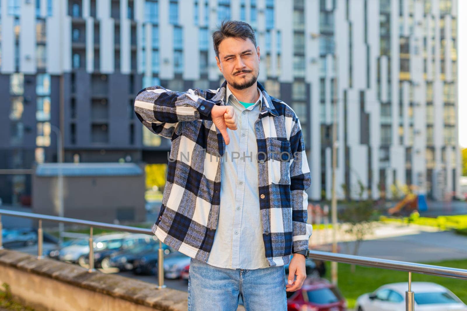 Dislike. Upset Caucasian mature man showing thumb down sign gesture, expressing discontent disapproval, dissatisfied bad work, mistake outdoors. Displeased guy tourist standing on urban city street.