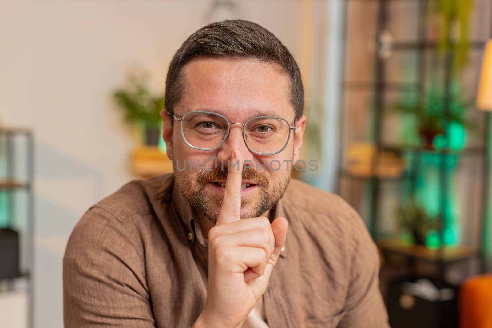 Shh be quiet please. Caucasian young businessman presses index finger to lips makes silence gesture sign do not tells secret at home office desk. Adult man with laptop in living room in apartment.
