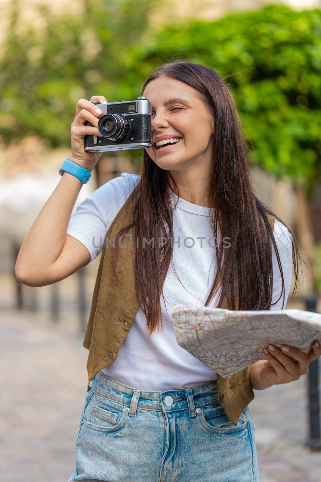 Caucasian young woman tourist traveling on weekends exploring town looking city map, making photo pictures on retro vintage camera outdoors. Happy adult lady traveler on urban city street. Lifestyles.