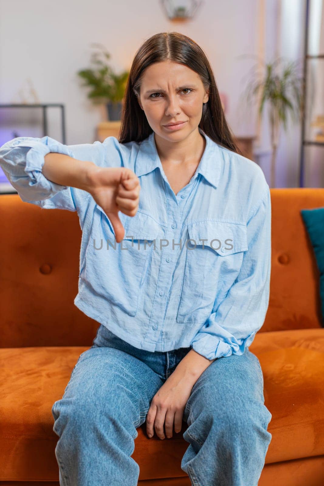 Dislike. Upset unhappy young Caucasian woman showing thumbs down sign gesture, expressing discontent, disapproval dissatisfied bad work at home apartment indoors. Displeased girl in room on sofa couch