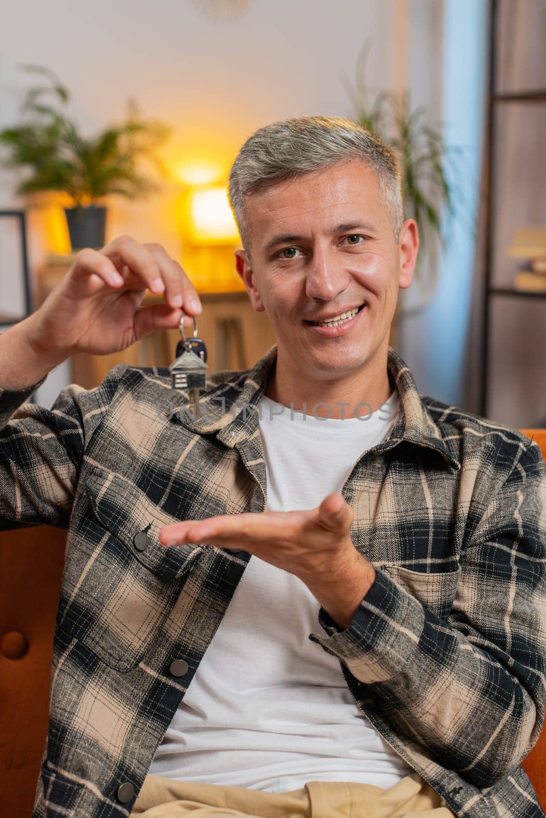 Happy Caucasian young man with gray hair real estate agent lifting hand showing the keys of new home house apartment, buying or renting property, mortgage loan investment at modern home room apartment