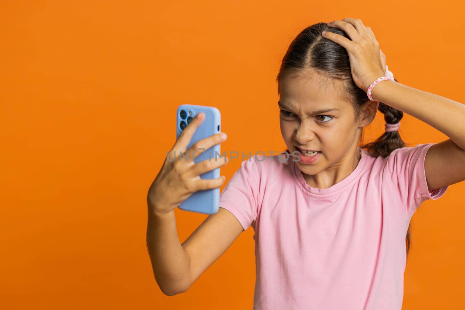 Upset sad preteen child girl kid use smartphone typing browsing, play game, loses, surprised by sudden lottery results, bad fortune, loss, fail, unlucky news. Sad children on orange background indoors