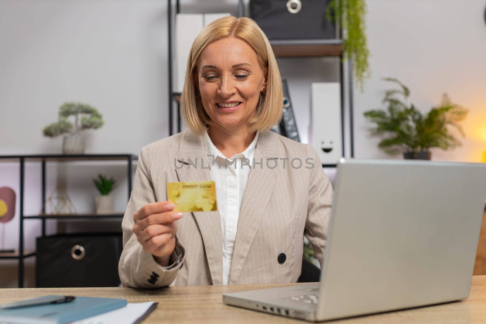 Happy Caucasian businesswoman using bank credit card and laptop for online shopping payments at home office. Business transaction. Smiling girl freelancer purchase with computer E-banking app service.