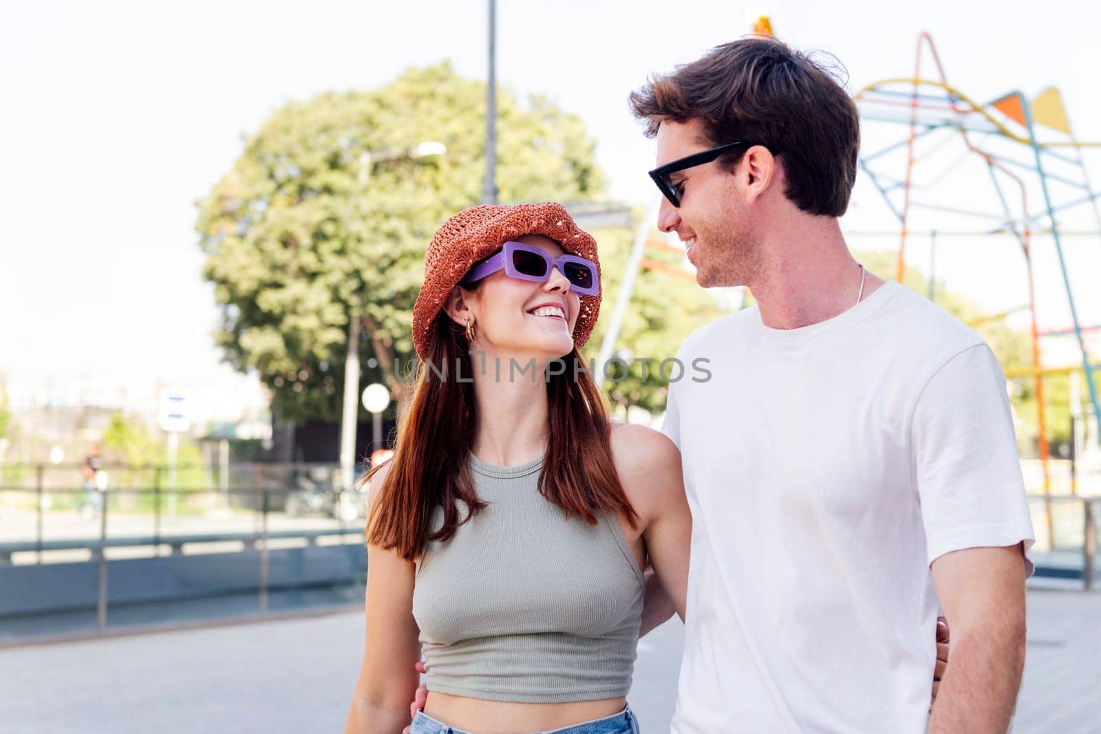 young couple smiling happy looking each other during a walk, the woman is wearing a hat and sunglasses, concept of youth and romance, copyspace for text