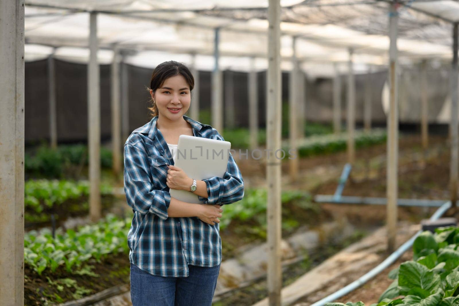 Portrait of confident female farmer holding laptop standing in organic farm.