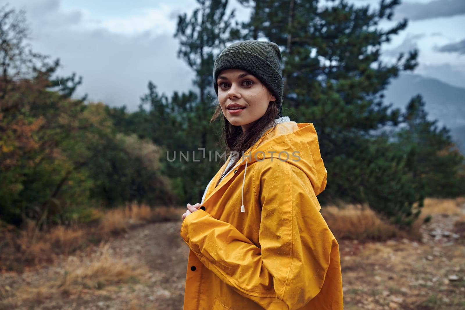 A woman in a yellow raincoat standing on a trail, surrounded by majestic mountains, ready for a hiking adventure