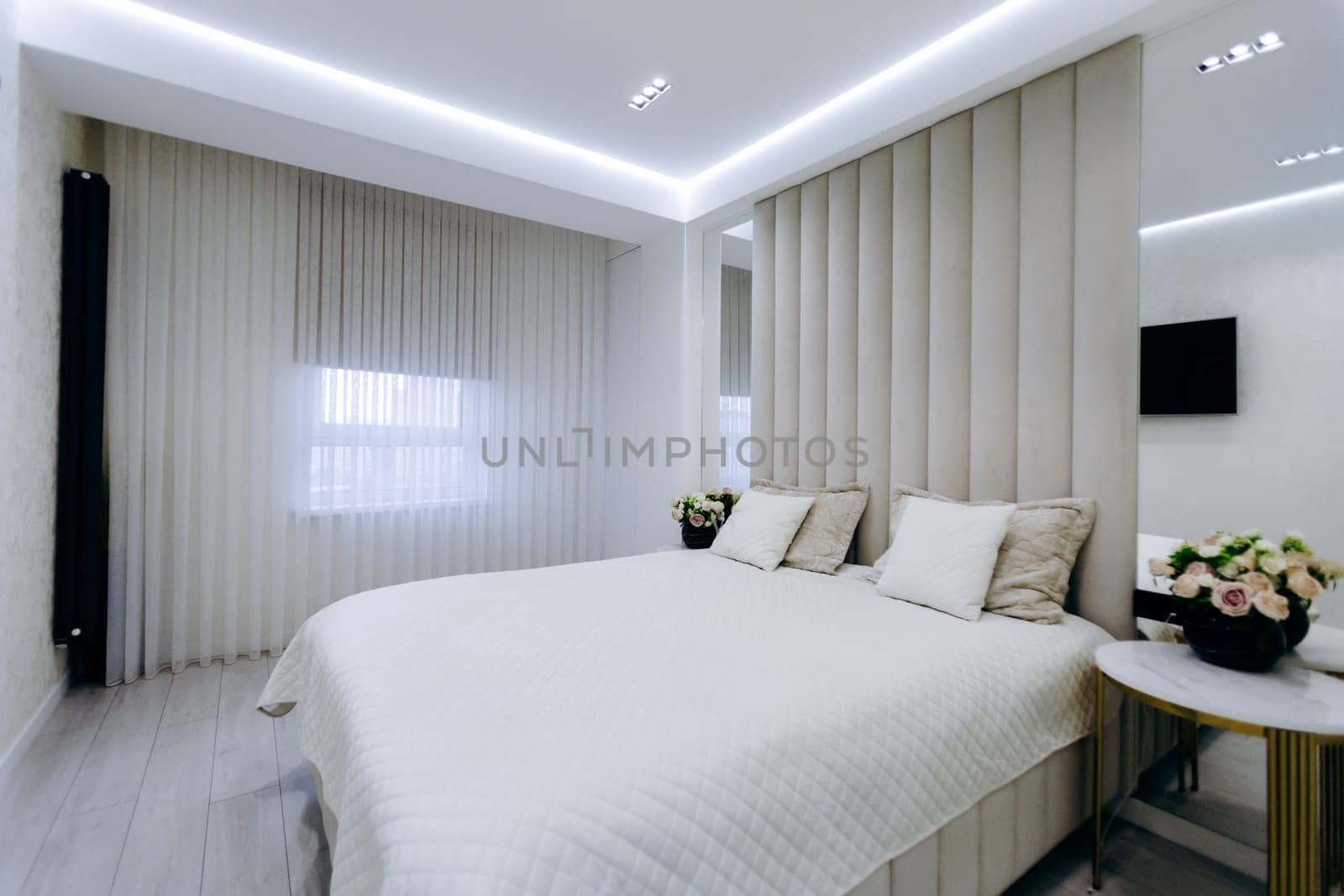 A cozy bedroom featuring a comfortable bed, a stylish nightstand, a decorative mirror, and an entertainment television set
