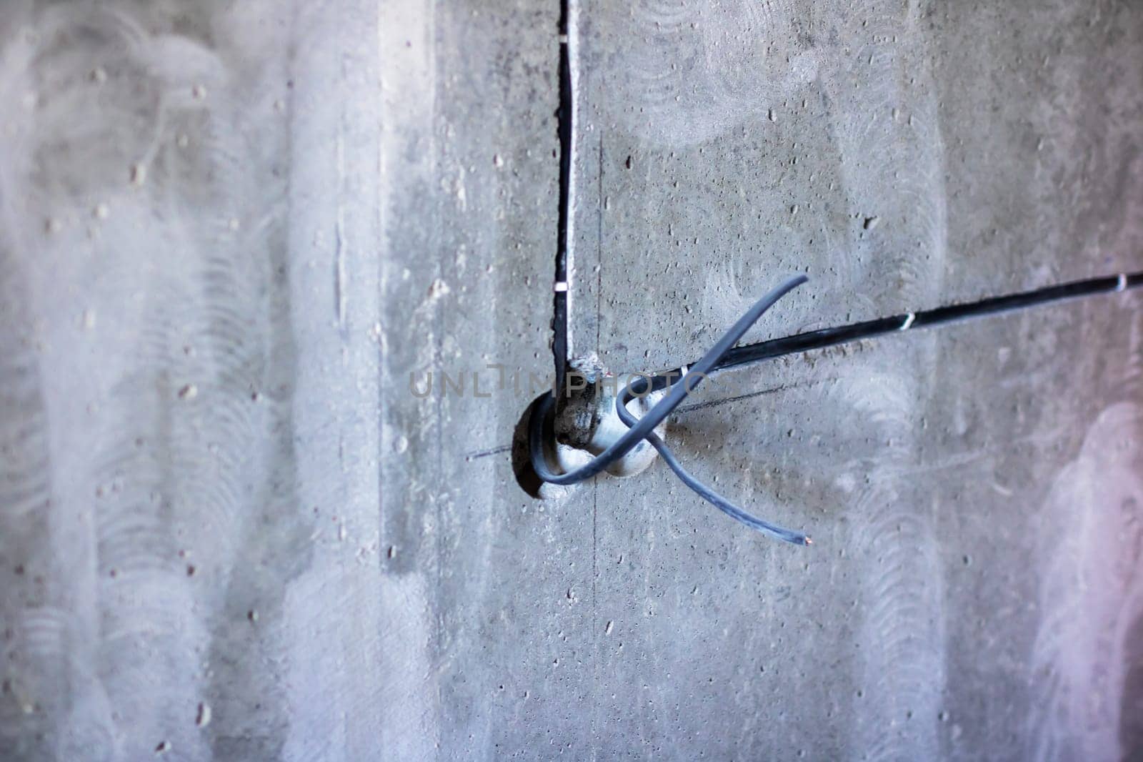 There is a noticeable hole present in a concrete wall, and from this opening, various wires are protruding outward from inside it
