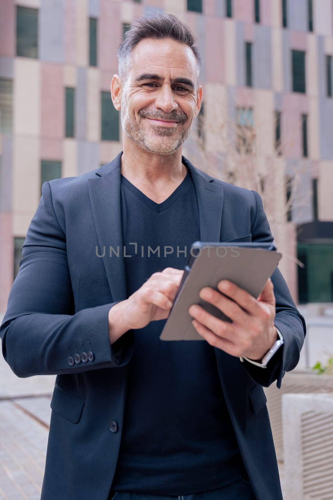 Confident mature businessman working on tablet outside a modern office building. looking at camera. Urban setting Ideal for business, technology, productivity, and professional lifestyle themes