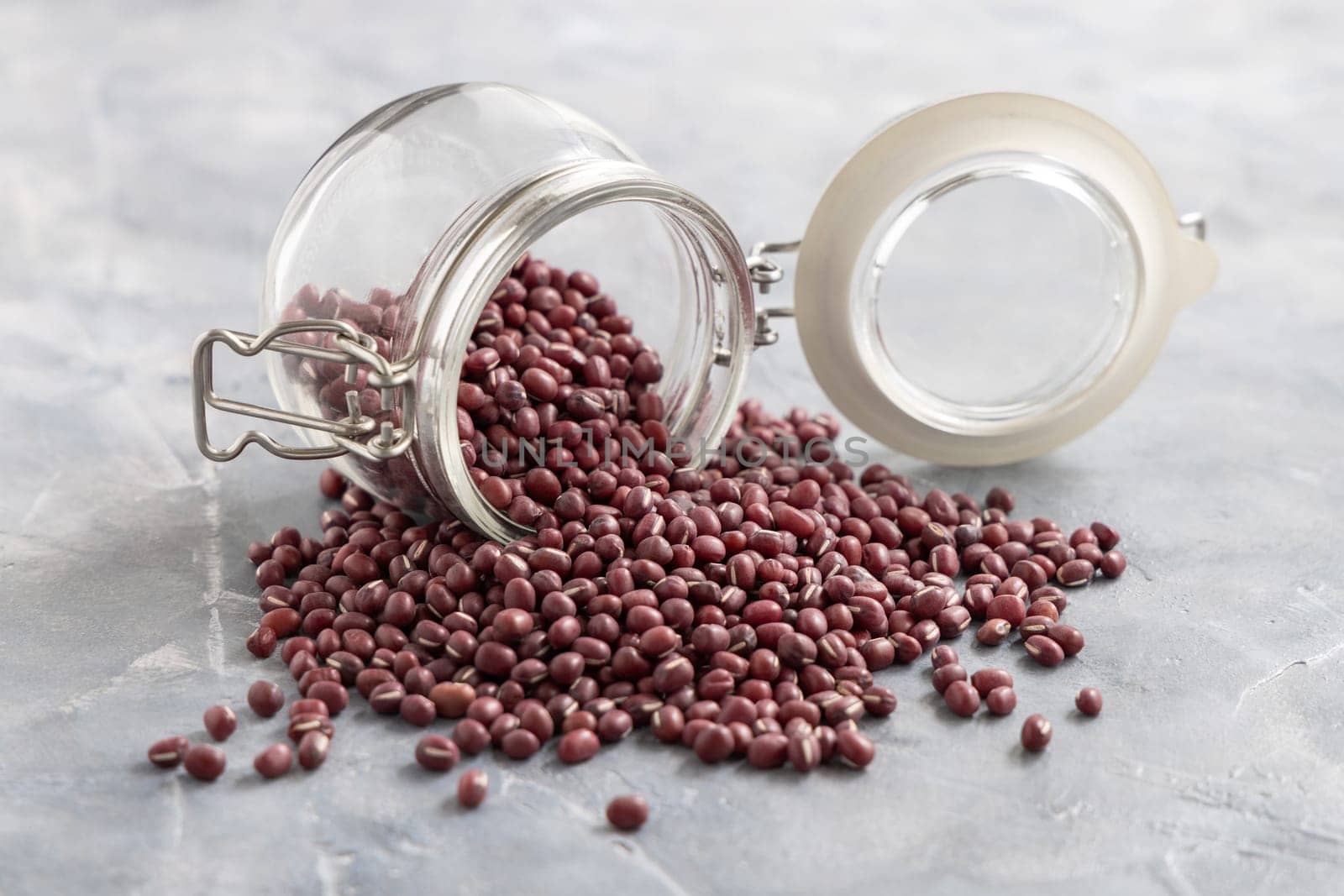 Opened glass jar full of dried azuki beans on gray table closeup. Healthy vegetarian food, legumes protein source. Traditional East Asiancousin ingredient