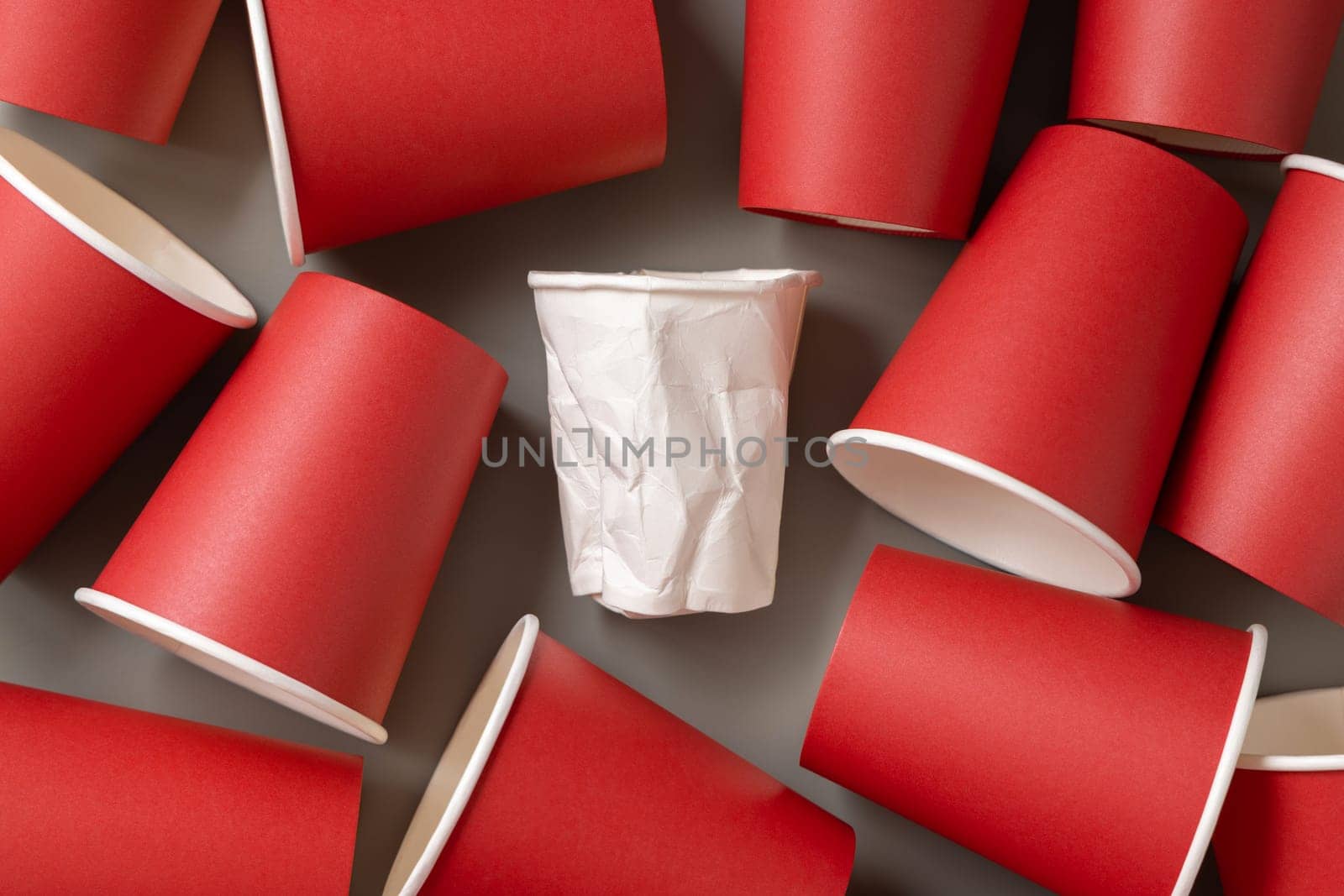 Disposable new red paper cups and crumpled used white one on gray top view. Empty single-use cardboard coffee cups flat lay. Consumerism concept in modern world