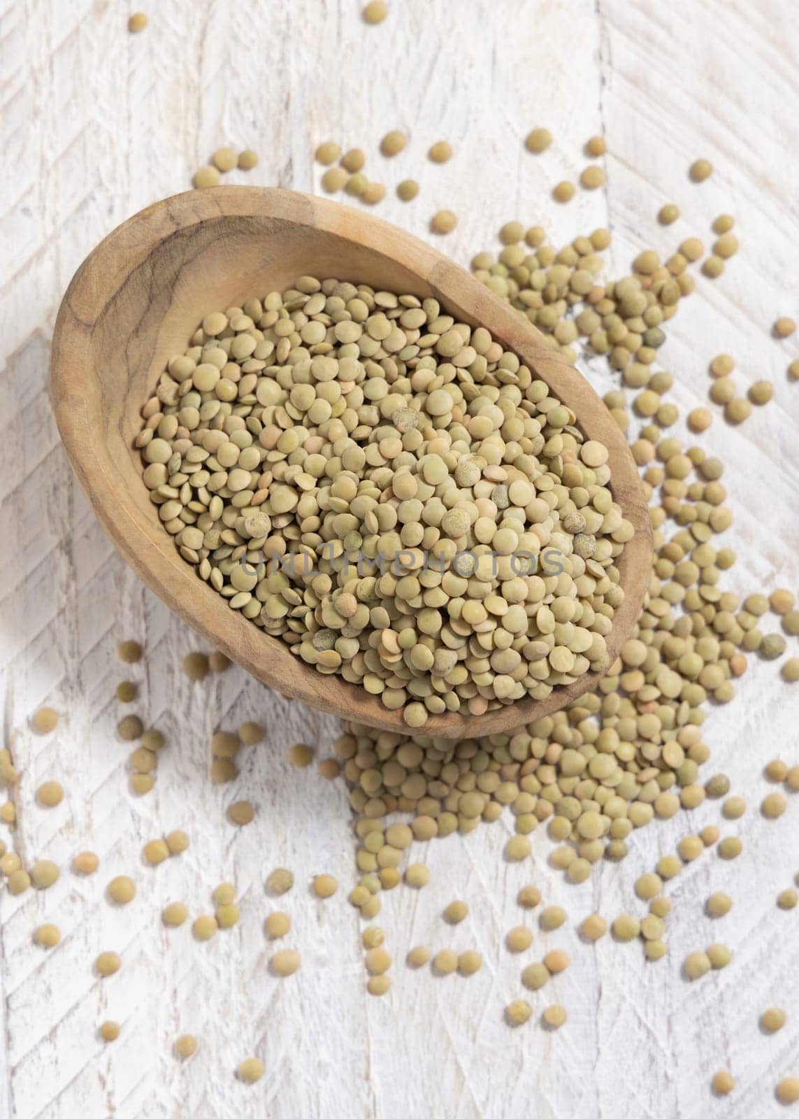 Wooden bowl full of dried green lentils on white table top view. Healthy raw vegetarian food, legumes plant-based protein source. Traditional mediterranean uncooked cousin ingredient