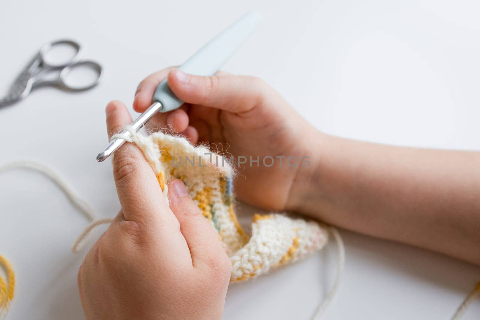 Close up of young caucasian child crocheting with yellow and white yarn.