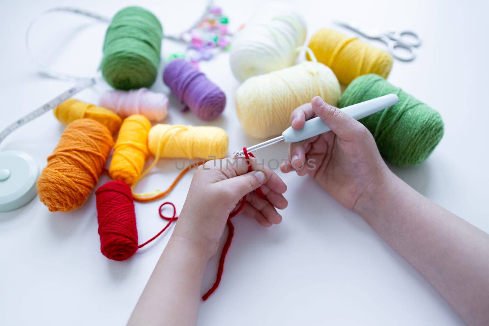 Child crocheting with colorful yarn balls and crochet hook.