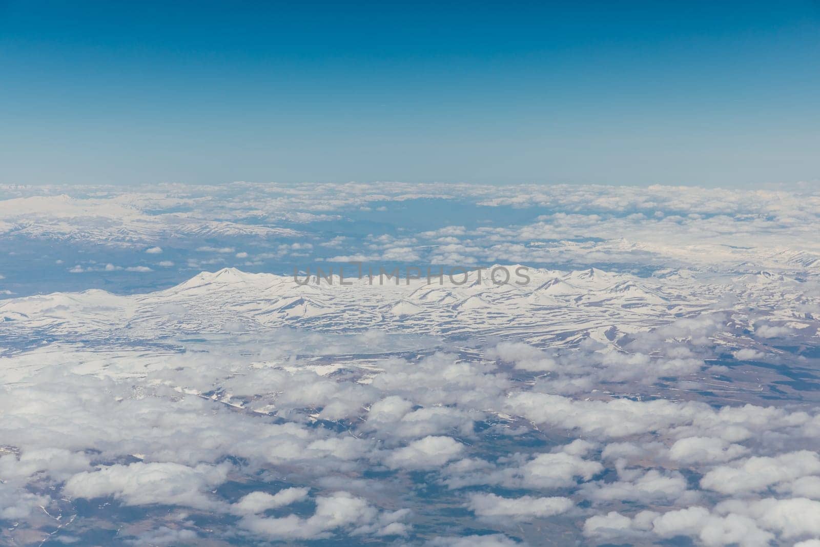 landscape on snowy mountains with clouds from the window of an airplane