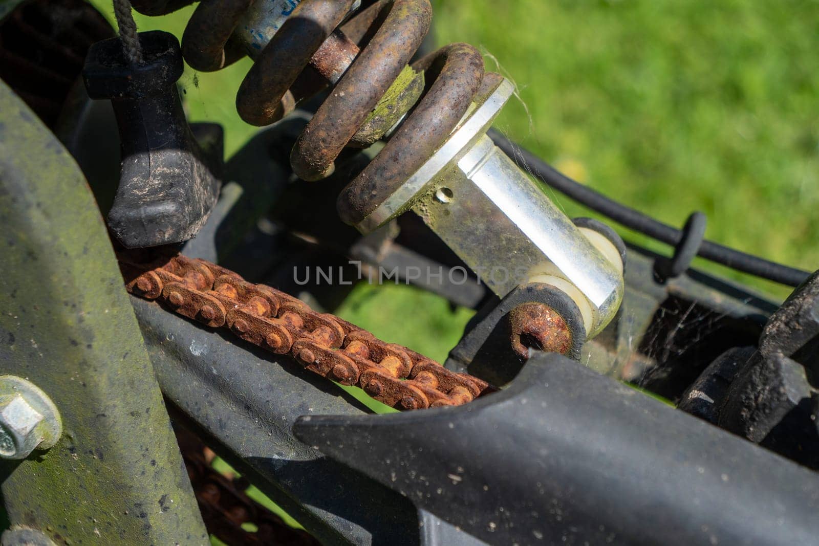 A rusty chain is attached to a bike. The chain is old and worn, and it is attached to the bike's rear end. The bike is parked in a grassy area, and the chain is visible in the foreground