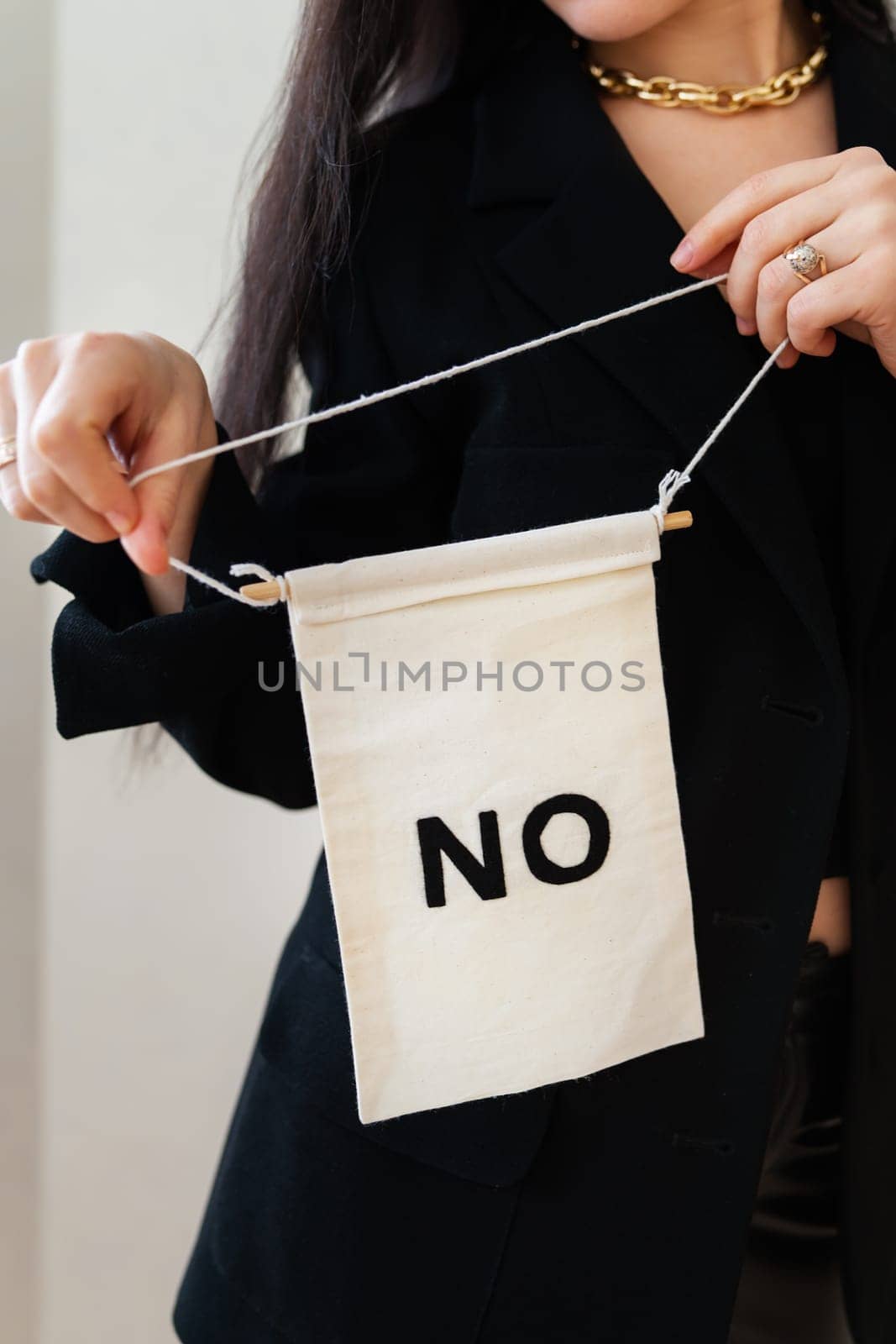 A woman in a black blazer resolutely holds a small banner reading 'NO', conveying a message of refusal or dissent.