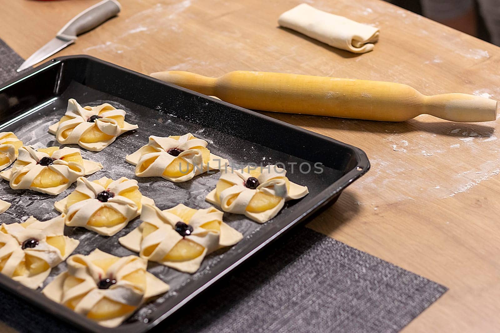 Puff pastry with pineapple wedges wrapped and cherry on top, on the baking tray in the kitchen counter top