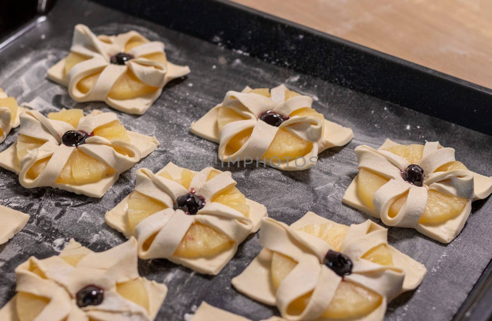 Puff pastry with pineapple wedges wrapped and cherry on top, on the baking tray in the kitchen counter top