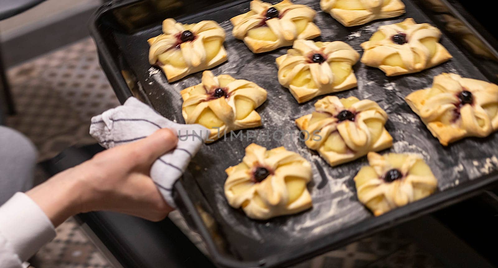 A woman picks baking tray with puff pastry with pineapple wedges wrapped and cherry on top from the oven