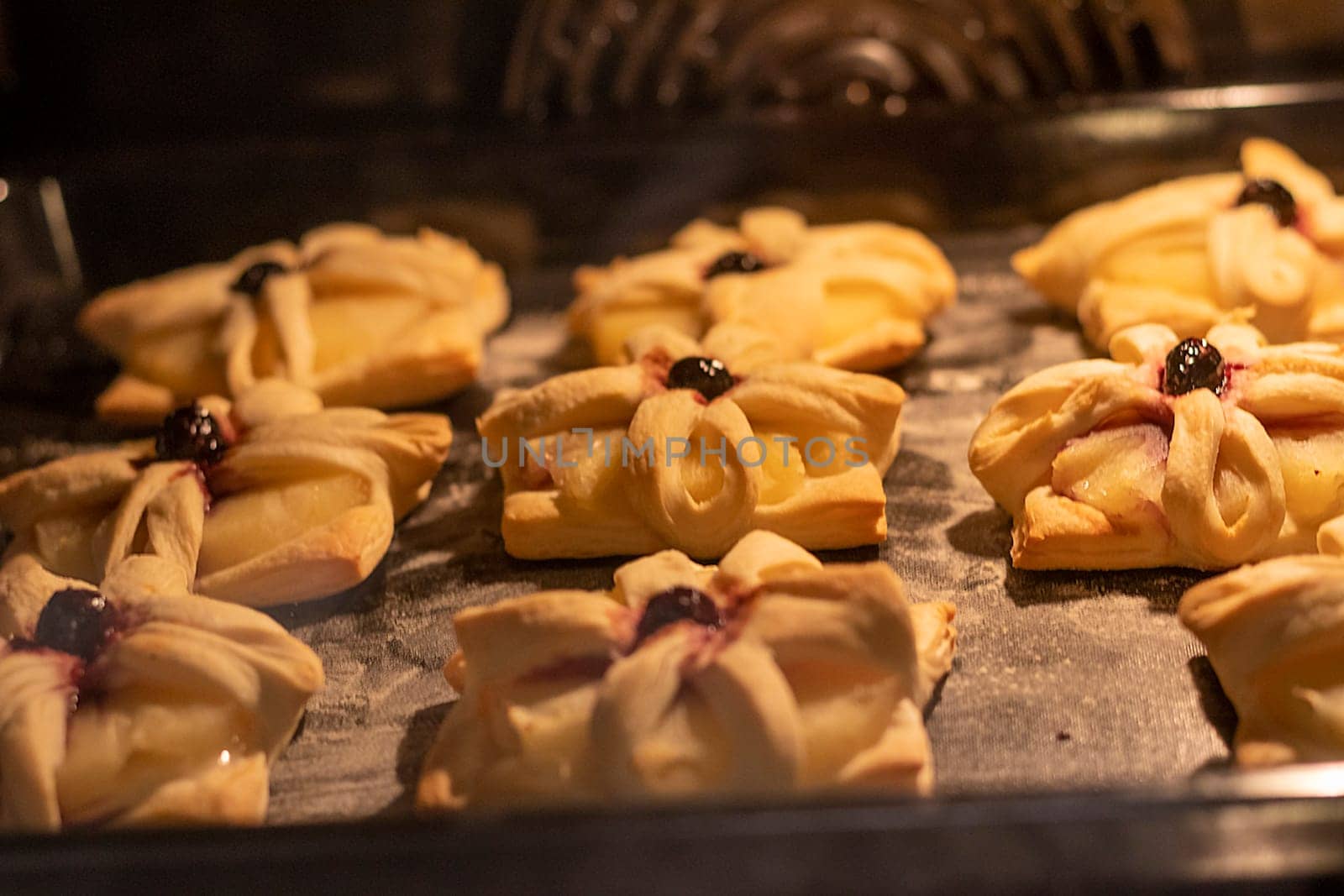 Puff pastry with pineapple wedges wrapped and cherry on top, on the baking tray baking in the oven