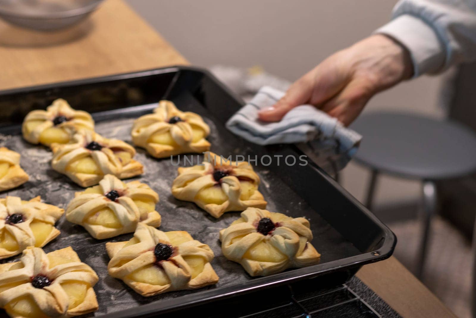 A woman places baking tray with with puff pastry with pineapple wedges wrapped and cherry on top from the oven to the kitchen counter top