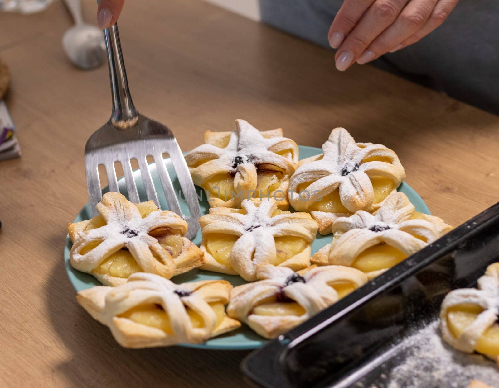 A woman pick the fruit puff pastries with spatula from baking tray and places them on ceramic plate