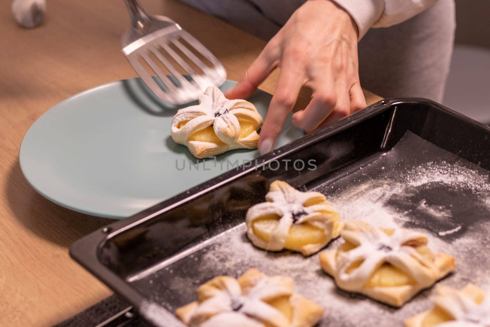 A woman pick the fruit puff pastries with spatula from baking tray and places them on ceramic plate