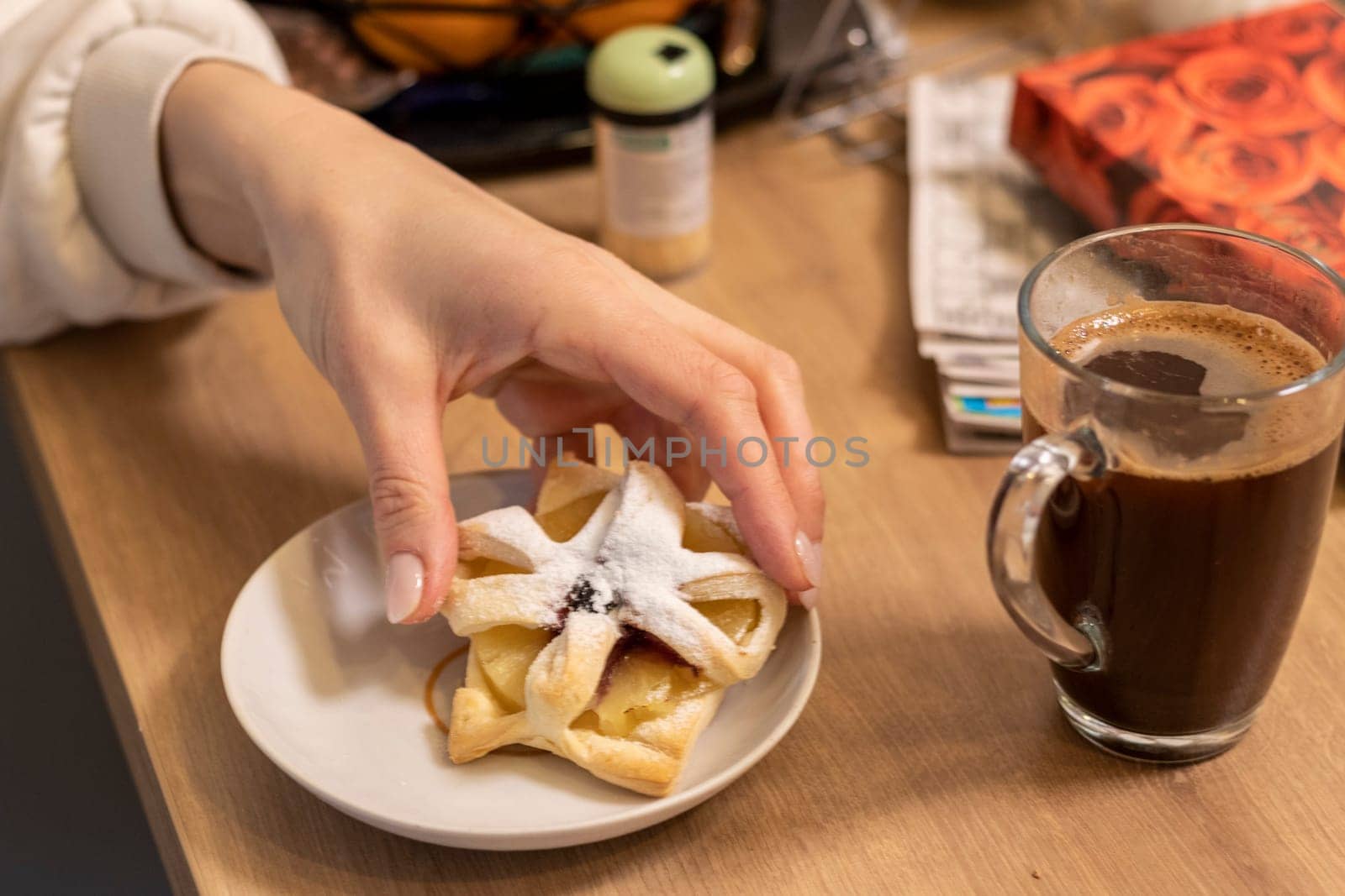 A woman picks freshly baked fruit puff pastry on the ceramic plate next to hot cup of coffee