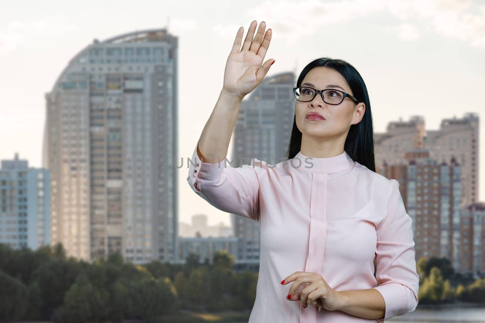 Young asian woman is touching an invisible virtual with her hand. Urban cityscape background.