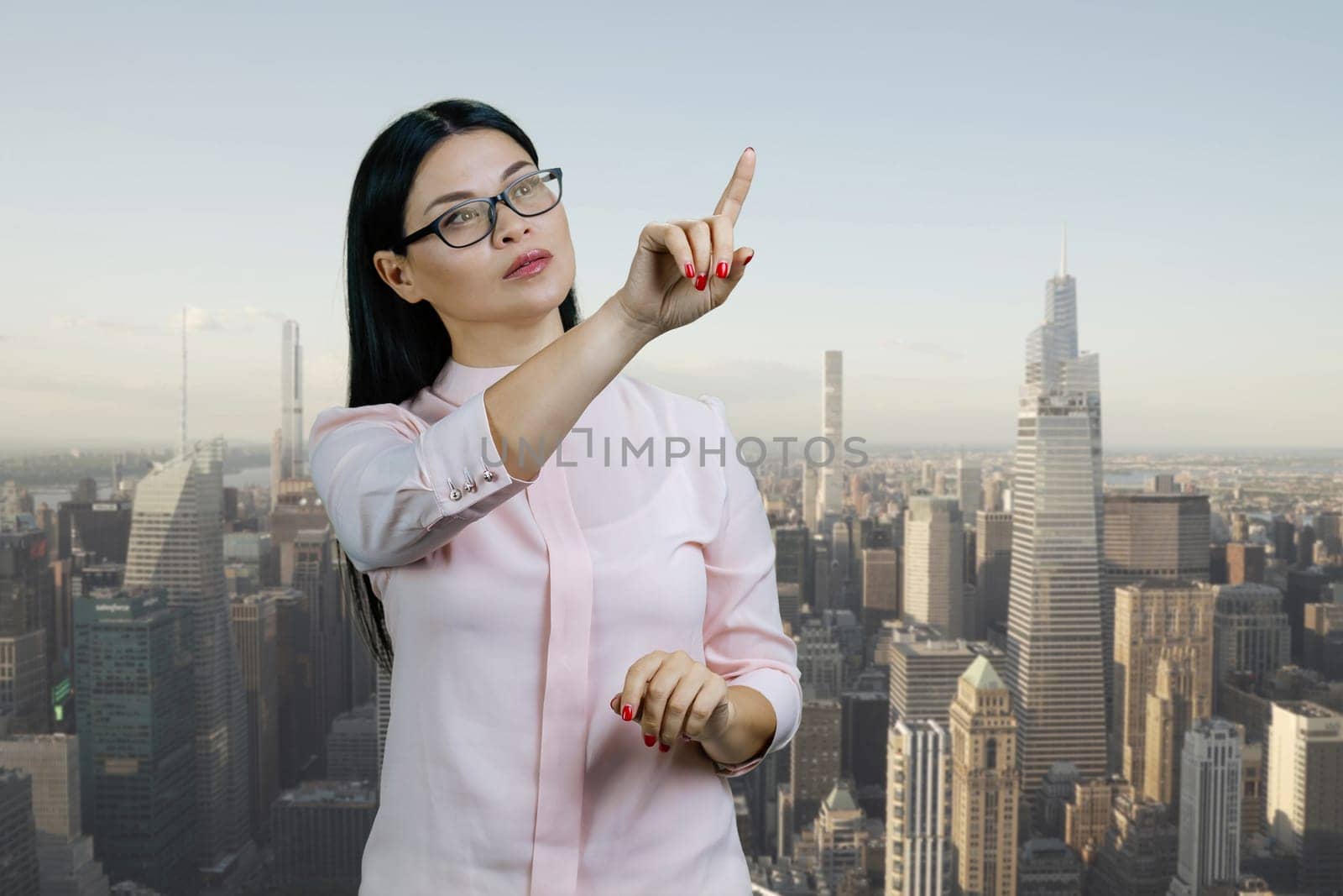 Asian businesswoman is pointing at copy space using invisible virtual screen. Urban cityscape background.