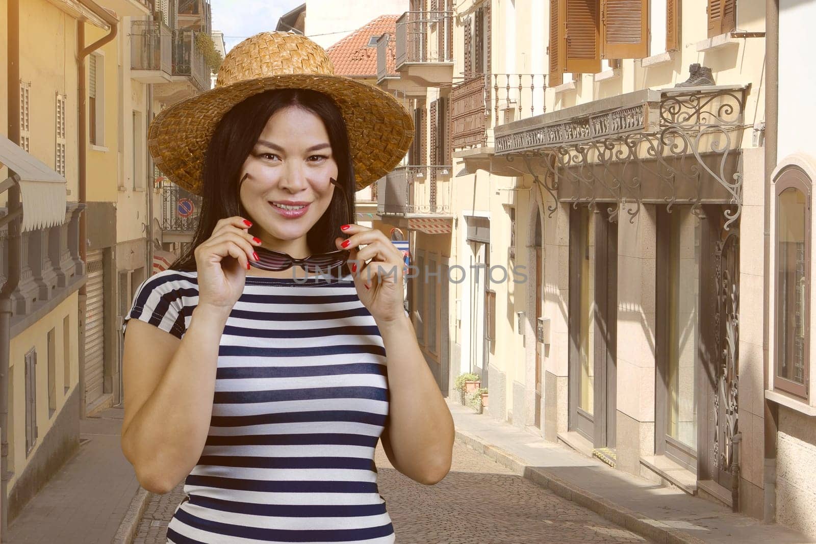 Asian female tourist is wearing straw hat. European italian street background.